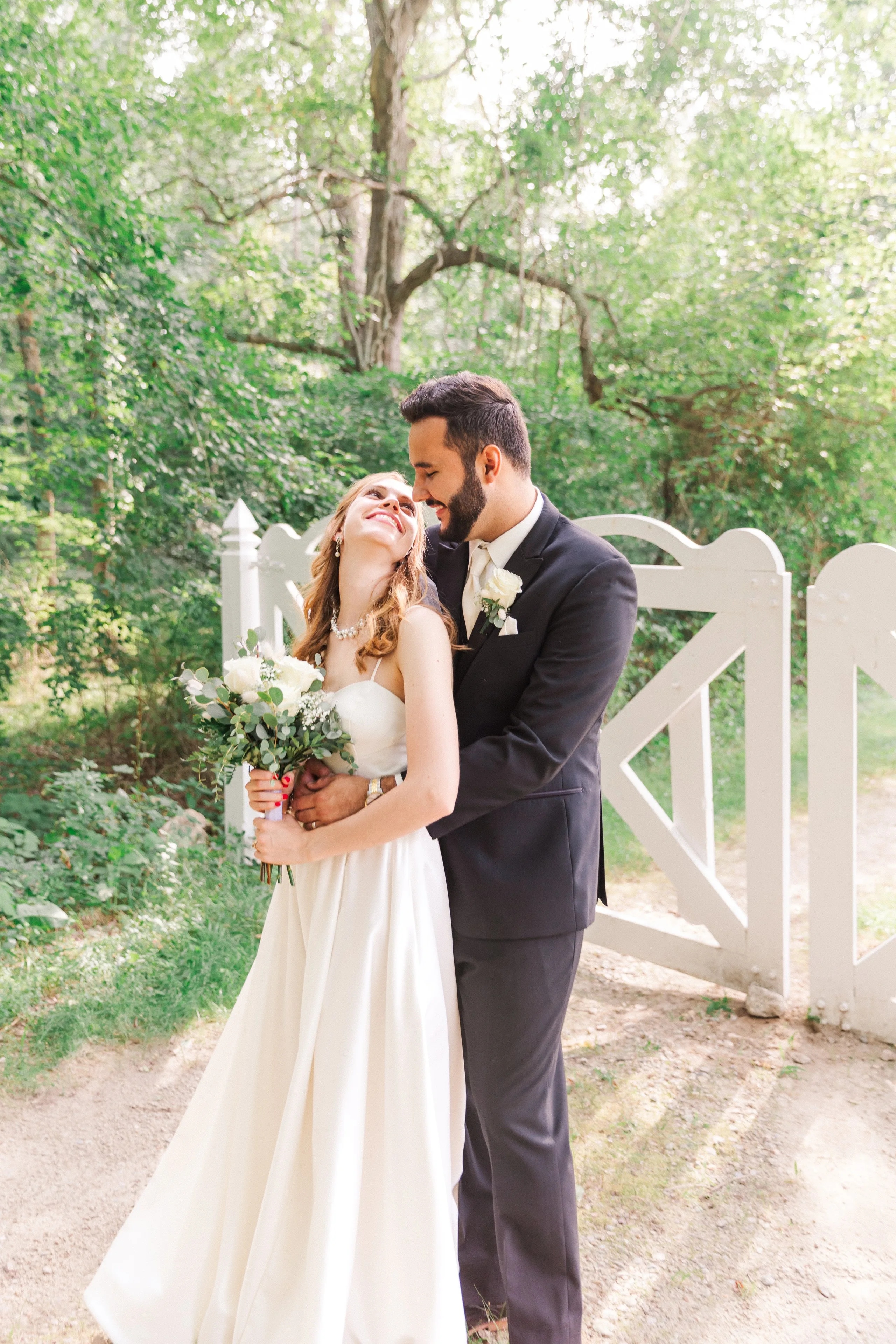Couple nuzzling at a white garden gate in warm golden light, by Nissi Photo